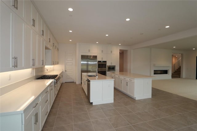 kitchen featuring an island with sink, sink, white cabinets, built in appliances, and light tile patterned floors