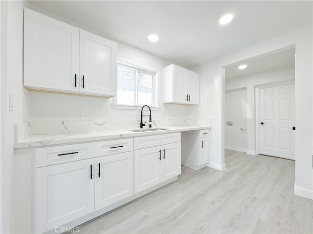 kitchen featuring light stone counters, light wood-type flooring, white cabinetry, and sink