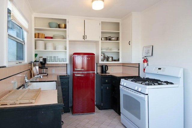 kitchen featuring backsplash, white cabinets, sink, white gas range, and light tile patterned floors