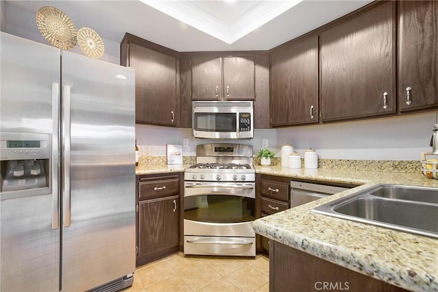 kitchen with dark brown cabinets, stainless steel appliances, light stone counters, and ornamental molding