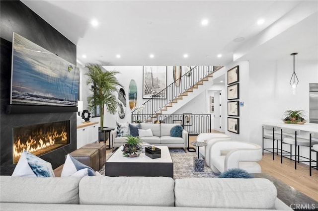 living area featuring a large fireplace, stairway, wood finished floors, and recessed lighting