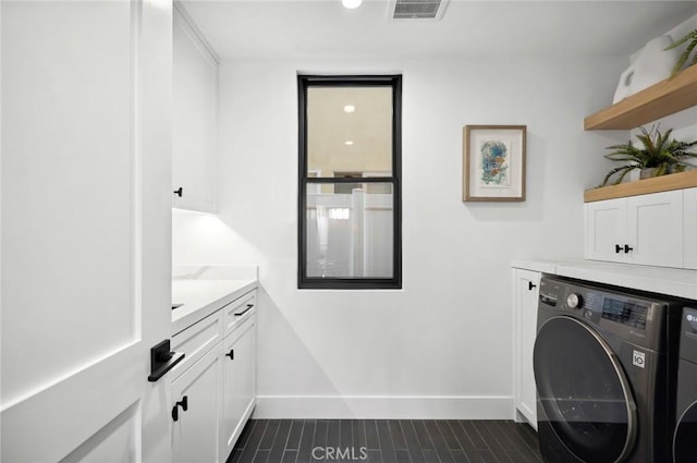 washroom with baseboards, cabinet space, visible vents, and washing machine and clothes dryer