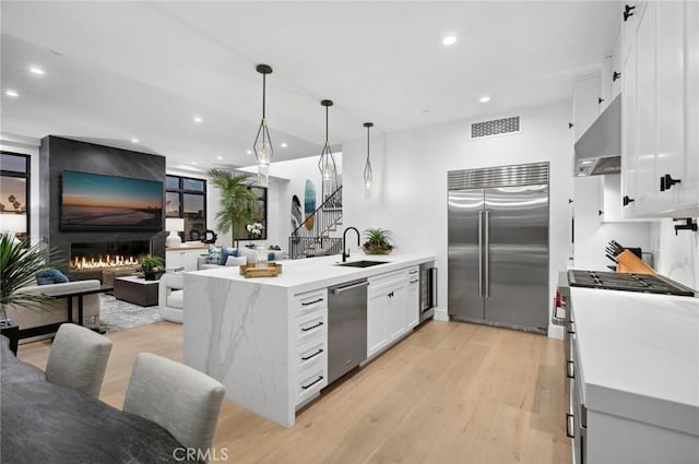 kitchen featuring under cabinet range hood, a peninsula, a fireplace, a sink, and high quality appliances