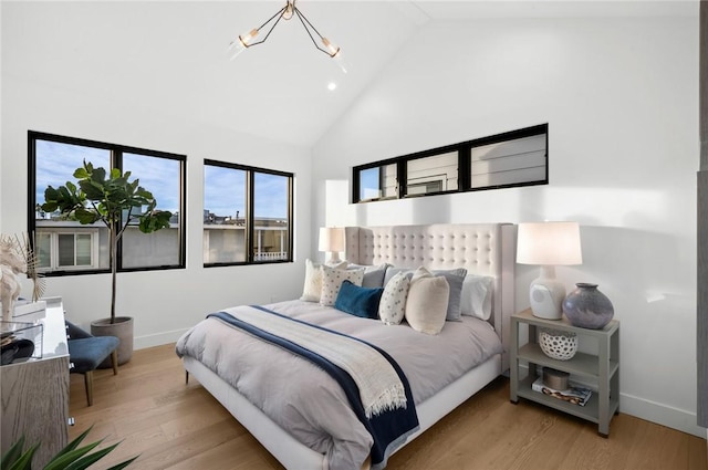 bedroom with baseboards, high vaulted ceiling, wood finished floors, and a notable chandelier