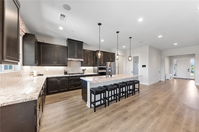 7631 Capstone Ct, Riverside, CA 92506 - kitchen featuring appliances with stainless steel finishes, light wood-type flooring, backsplash, dark brown cabinets, and a kitchen breakfast bar