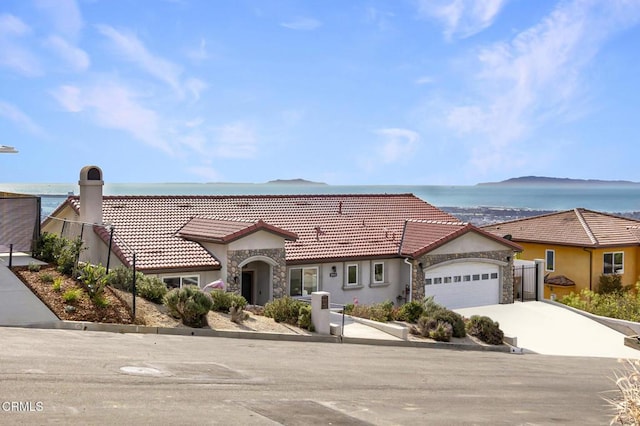 view of front facade with a garage, a water view, a tiled roof, and stone siding