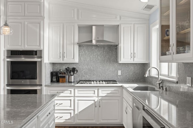 kitchen featuring visible vents, glass insert cabinets, a sink, wall chimney exhaust hood, and white cabinets