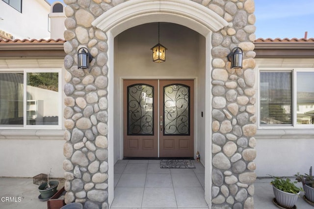 entrance to property with stucco siding, stone siding, and a tile roof