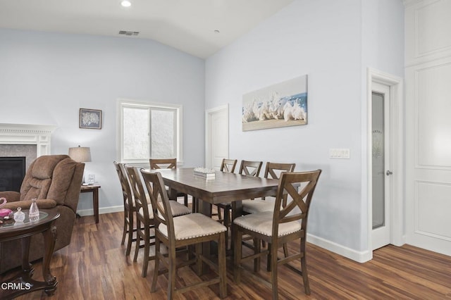 dining space featuring visible vents, a glass covered fireplace, vaulted ceiling, and dark wood-style flooring