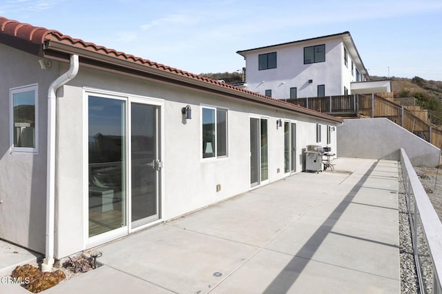 rear view of house featuring fence, a tiled roof, stucco siding, and a patio area