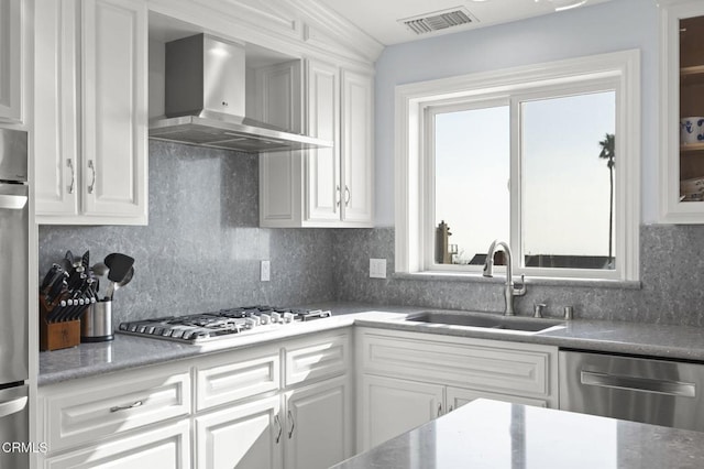 kitchen featuring visible vents, white cabinetry, a sink, stainless steel appliances, and wall chimney range hood