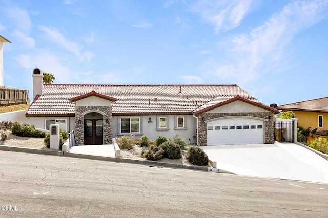 view of front of house with french doors, stone siding, a tiled roof, concrete driveway, and an attached garage