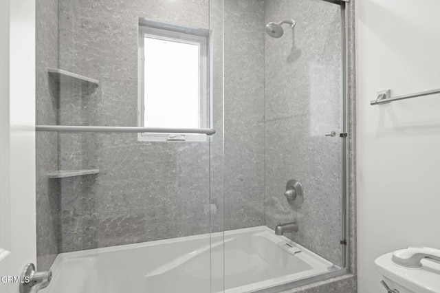 bathroom featuring toilet and shower / bath combination with glass door