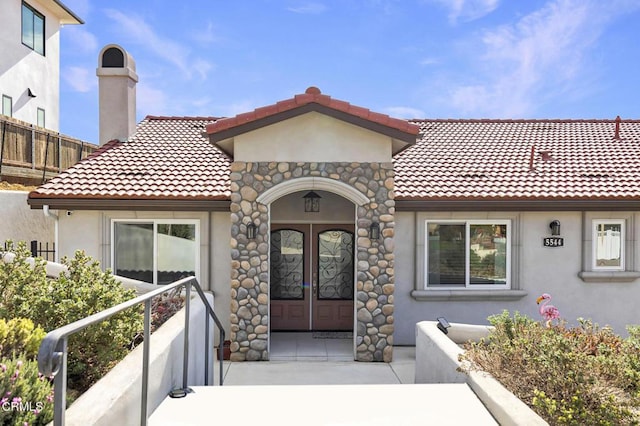 doorway to property featuring french doors, stucco siding, a chimney, and a tile roof