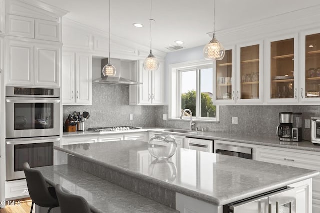 kitchen with a center island, glass insert cabinets, stainless steel appliances, wall chimney range hood, and white cabinets