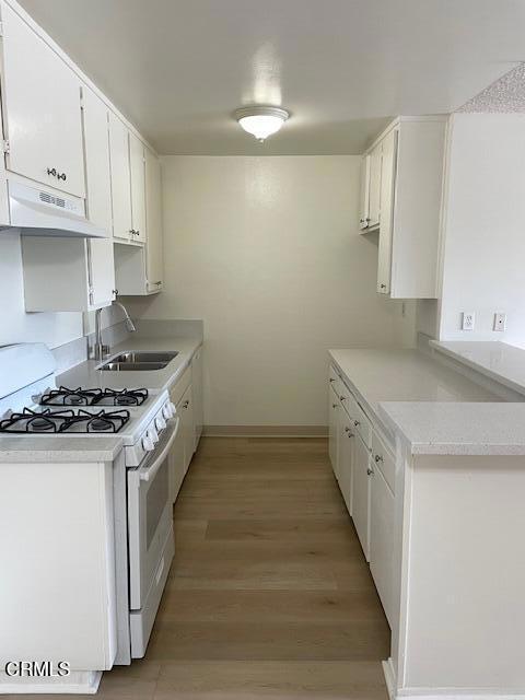 kitchen with white gas range oven, a sink, white cabinetry, and under cabinet range hood