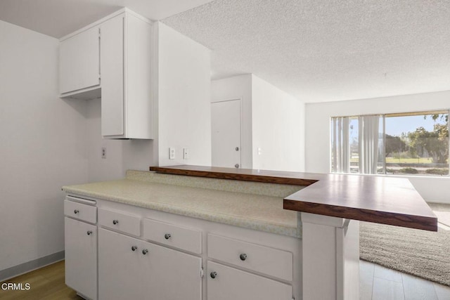 kitchen with light wood-style flooring, white cabinets, a textured ceiling, and light countertops