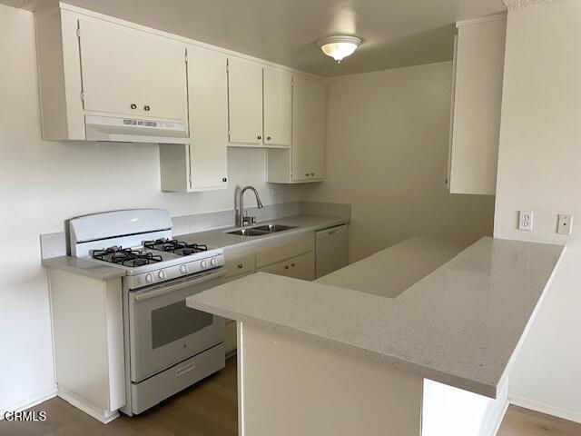 kitchen featuring under cabinet range hood, a peninsula, white appliances, a sink, and light countertops