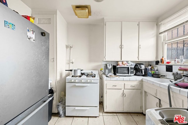 kitchen featuring white cabinets, tile counters, light tile patterned floors, and appliances with stainless steel finishes