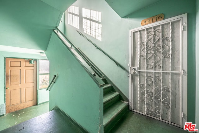 staircase featuring vaulted ceiling and concrete floors