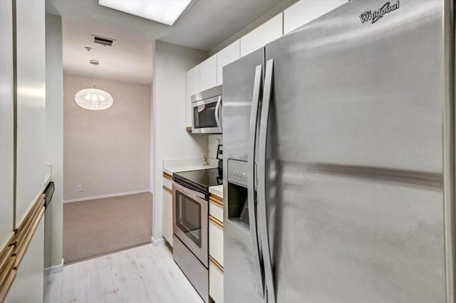 kitchen featuring white cabinetry, stainless steel appliances, decorative light fixtures, and light hardwood / wood-style flooring