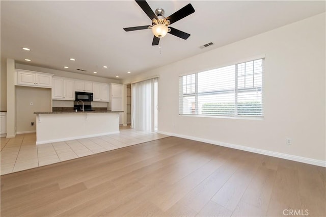 unfurnished living room with light wood-type flooring, ceiling fan, and sink