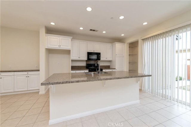 kitchen featuring black appliances, a center island with sink, sink, dark stone countertops, and white cabinetry