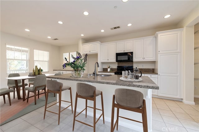 kitchen featuring an island with sink, sink, white cabinets, and black appliances