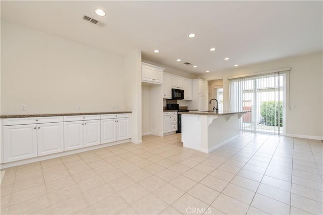 kitchen featuring white cabinetry, dark stone countertops, an island with sink, a breakfast bar area, and black appliances