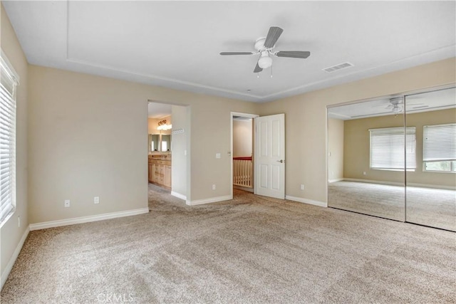 unfurnished bedroom with a closet, light colored carpet, ensuite bath, and ceiling fan