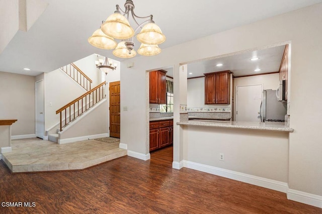 kitchen featuring dark wood-type flooring, appliances with stainless steel finishes, light stone counters, kitchen peninsula, and a chandelier