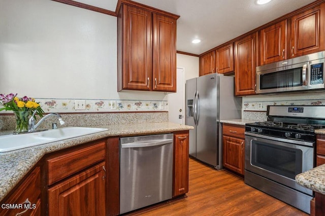 kitchen featuring sink, light stone counters, ornamental molding, appliances with stainless steel finishes, and hardwood / wood-style flooring