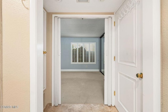 hallway with light carpet and a textured ceiling