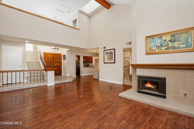 unfurnished living room with beamed ceiling, wood-type flooring, high vaulted ceiling, and a tiled fireplace