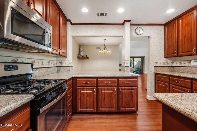 kitchen with appliances with stainless steel finishes, ornamental molding, dark wood-type flooring, decorative light fixtures, and an inviting chandelier