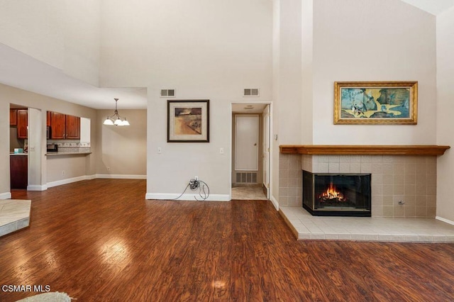 unfurnished living room with a fireplace, a high ceiling, hardwood / wood-style flooring, and a chandelier