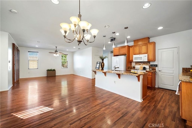 kitchen with ceiling fan with notable chandelier, white appliances, decorative light fixtures, a kitchen bar, and tasteful backsplash