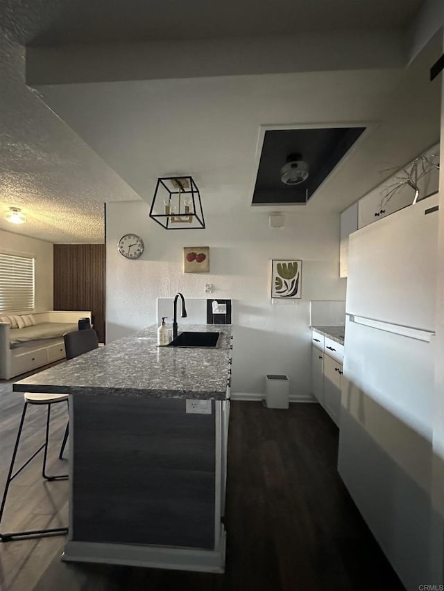 kitchen with stone counters, white cabinetry, sink, a breakfast bar area, and white fridge