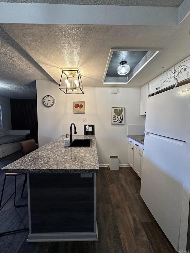 kitchen featuring stone countertops, white cabinetry, sink, white fridge, and a textured ceiling