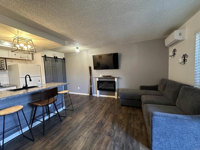 living room featuring sink, a textured ceiling, an AC wall unit, dark hardwood / wood-style floors, and a barn door