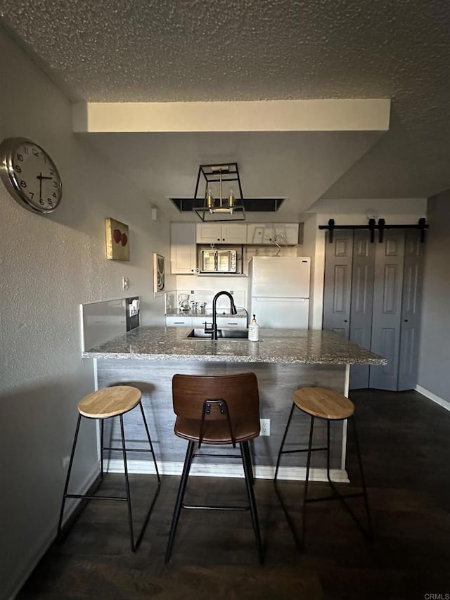 kitchen featuring a breakfast bar area, a barn door, kitchen peninsula, and white fridge