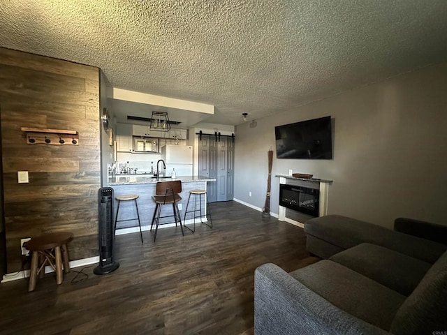 living room featuring a barn door, dark hardwood / wood-style flooring, a textured ceiling, and wood walls