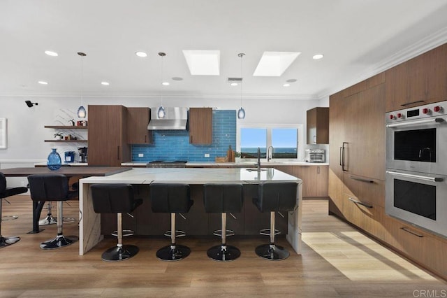 kitchen with a skylight, wall chimney exhaust hood, pendant lighting, and appliances with stainless steel finishes