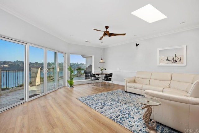 living room featuring a skylight, ceiling fan, light hardwood / wood-style flooring, crown molding, and a water view