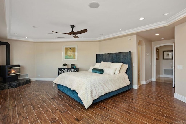 bedroom featuring a raised ceiling, a wood stove, ceiling fan, and ornamental molding