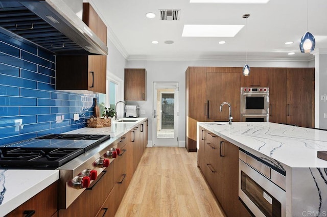 kitchen featuring a skylight, sink, wall chimney exhaust hood, stainless steel appliances, and pendant lighting