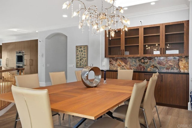 dining space featuring wood-type flooring, ornamental molding, and an inviting chandelier