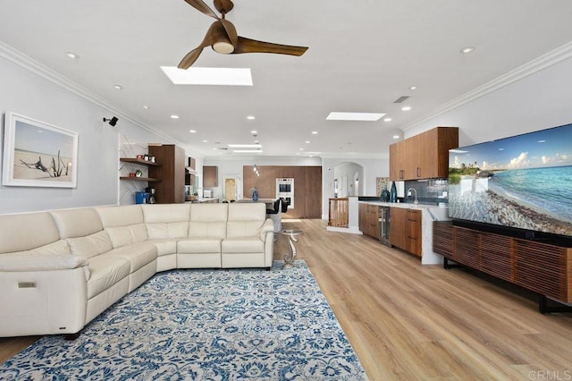 living room with a skylight, ceiling fan, beverage cooler, light hardwood / wood-style flooring, and crown molding