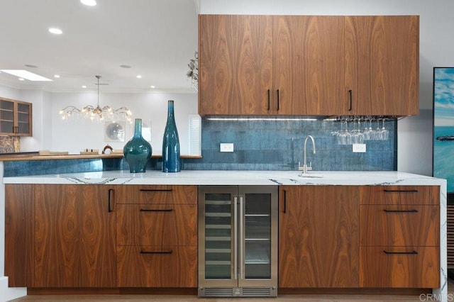 kitchen featuring beverage cooler, tasteful backsplash, light stone counters, crown molding, and decorative light fixtures