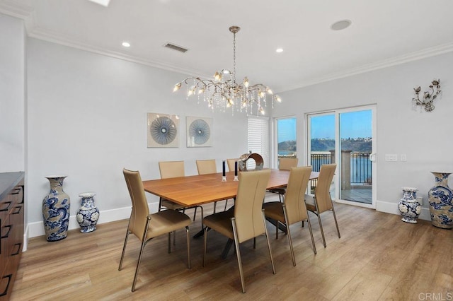 dining room featuring light wood-type flooring, ornamental molding, and an inviting chandelier